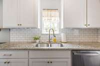 This kitchen shines with granite countertops, a stylish tile backsplash, and tons of natural light