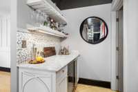 Wet bar with wine fridge, stunning countertops and tile backsplash with decorative cabinetry