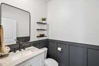 Half bath tucked away downstairs with board and batten walls, new vanity with marble top, and decorator shelves and new mirror.