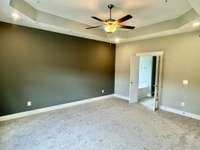 Owner's suite featuring tray ceiling, led lights, fan and dark grey accent wall.