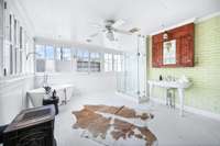 A charming primary bath! Lots of natural light with original windows, free standing soaking tub, separate frameless glassed shower, gorgeous wash stand, exposed brick, and white washed hardwood floors.