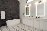 The spa-inspired primary bath offers an extended dual vanity, a relaxing soaking tub, and a striking floor-to-ceiling stone wall accent.