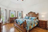 Primary bedroom with vaulted ceiling, hardwood floors, and abundant natural light