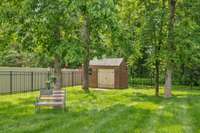 Mature trees provide shade near the charming brick utility shed.