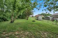 The backyard is shaded by mature trees, perfect for relaxing, gardening, or playing outside.