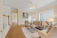 A warm and welcoming living room, where a ceiling fan keeps the air cool and comfortable. Extra-wide crown molding and wood details add a touch of charm and character to the space. (Virtually staged)