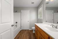 Ensuite bath in the primary bedroom features vinyl hardwood floors, oak vanity, neutral paint and a separate tub/shower.