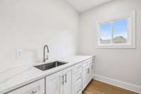 Utility room with cabinetry, sink, and matching quartz top.
