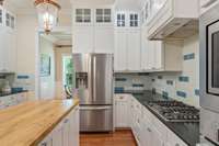 Gas cooktop, Bosch stainless appliances, ceramic backsplash, and upper box cabinets with glass door fronts.