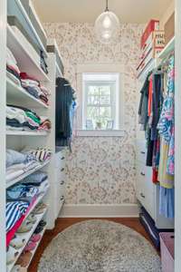 Walk in closet currently decorated and used as the feminine space with pink hues of wallpaper and built in drawers for dresser use