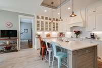 The gourmet kitchen has high-end appliances and bespoke, custom cabinets that complement the home’s elegant aesthetic. The glass-front units feature clear glass shelving that allows lighting to illuminate the entire interior.