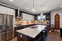 Gourmet kitchen with stainless steel hood vent, stainless steel appliances, brick backsplash, open wood shelving and quartz countertops.