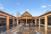View of the Back of the Main Lodge showing all garage doors open and outdoor kitchen and lounge area. To the left is the game/Armory room and to the right is the Archery Simulator.