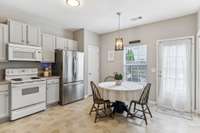 Bright and airy eat-in kitchen with updated light fixture, stainless steel refrigerator, and easy access to the private patio—perfect for morning coffee or casual dining.