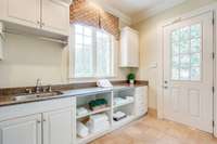 This laundry room has a sink, granite counter, open shelving, room for a refrigerator and access to the side friends entrance door of the home. This door has a custom lock for additional safety.