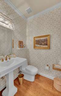 The main floor half bath features designer wallpaper, a gorgeous pedestal sink, & brushed gold fixtures.