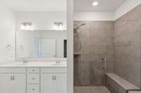 Double vanity, tiled shower, bench for sitting.