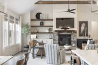 This living room features wood flooring, exposted wood beams, a stacked stone gas fireplace, floating wood shelving and built-in cabinets.