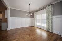 Large dining room with wainscoting, plantation shutters, hardwood floors and curtains that remain, if desired.