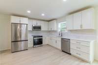 Stainless steel appliances, new cabinets, flooring, quartz countertops, and tile backsplash