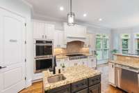 A chef’s dream, this kitchen is appointed with white cabinetry, a large center island complete with sink and drawers for accessibility, and overhead lighting that is both modern and classic.
