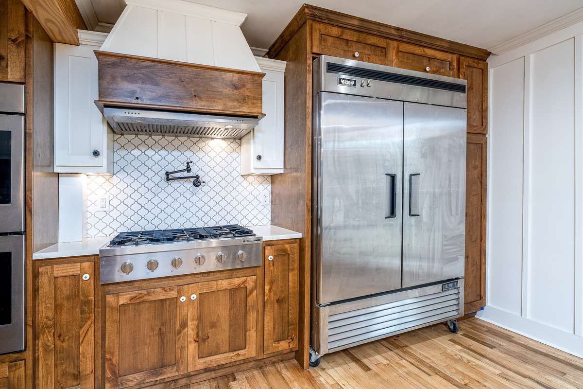 Pot Filler over Gas Stove, Commercial Stainless Steel Refrigerator, Custom Tiled Backsplash and Stove Hood