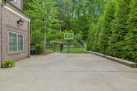 Side driveway with basketball hoop, access to backyard space and pool house.