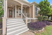 An inviting front porch with wide steps, wood railings, and a rich wood front door, perfect for relaxing with morning coffee.