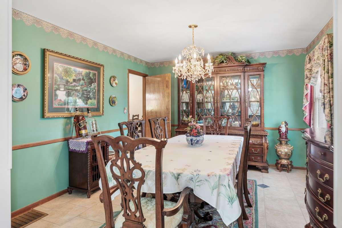 Formal dining room with elegant chandelier, tile floors, and abundant natural light—flows seamlessly into both the living room and kitchen for easy entertaining.