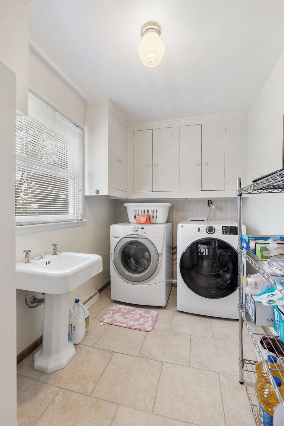 Bright laundry room with tile floors, built-in cabinetry, utility sink, and a large window—offering convenience and plenty of natural light for daily chores.