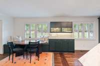 A built in seating area is framed by windows and flanked by a server area with glass cabinets above