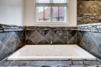 Deep jetted soaking tub set in natural stacked stone, accented by custom tilework—perfect for a relaxing spa-like retreat.