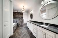 Luxurious master bath with custom stonework, featuring a spa-style walk-in shower with dual rainfall showerheads and an elegant soaking tub.