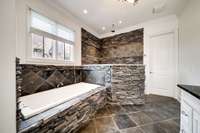 Luxurious master bath with custom stonework, featuring a spa-style walk-in shower with dual rainfall showerheads and an elegant soaking tub.