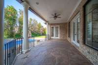 Spacious covered patio with stamped concrete, ceiling fan, and French doors overlooking a private backyard with pool and outdoor fireplace—perfect for relaxing or entertaining.
