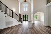 Impressive two-story foyer showcases a grand iron entry, soaring ceilings, and expansive windows—beautifully complemented by newly installed wide-plank flooring that extends into the formal dining room.