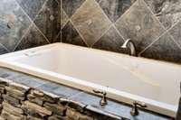 Deep jetted soaking tub set in natural stacked stone, accented by custom tilework—perfect for a relaxing spa-like retreat.
