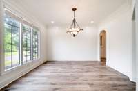 Elegant formal dining room with oversized windows for natural light, detailed crown molding, and easy flow to the kitchen through an arched entryway.