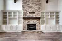 Soaring stone fireplace with rustic wood mantle anchors the living room, flanked by custom built-in shelving and cabinetry—perfect for displaying art, books, or media.