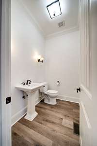 This is a well-appointed powder room featuring a pedestal sink with classic lines and oil-rubbed bronze fixtures. The warm-toned luxury vinyl plank flooring adds richness and continuity from the main living spaces.