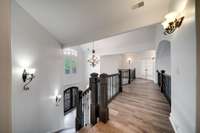 This elegant upper landing features rich wide-plank hardwood floors, iron balustrades, and sophisticated lighting, creating a refined connection between living spaces.