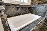 Deep jetted soaking tub set in natural stacked stone, accented by custom tilework—perfect for a relaxing spa-like retreat.