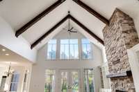 Soaring ceilings with exposed wood beams and a grand stone fireplace create a dramatic focal point in this light-filled living room.