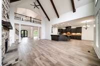 Open-concept layout showcases dramatic vaulted ceilings with exposed beams, flowing seamlessly from the stone fireplace living area into a chef’s kitchen with granite counters and custom cabinetry.