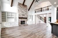 Stunning great room with stone fireplace, custom built-ins, exposed beams, and wood post staircase—set beneath soaring ceilings with designer finishes throughout.