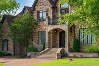 Grand brick staircase leads to double iron doors beneath a graceful arched entry—an impressive welcome that blends timeless craftsmanship with luxury design.