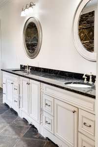 Elegant dual vanities with rich marble countertops, detailed millwork cabinetry, and framed oval mirrors—designed for both luxury and functionality.
