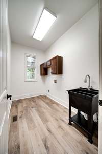 This is a laundry room featuring a utility sink with a high-arc faucet, and upper cabinetry for storage. The space is plumbed and wired for a washer and dryer and benefits from natural light through a window.