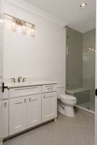 This well-appointed bathroom features a sleek vanity with quartz countertops, a walk-in shower with built-in shelving, and modern fixtures throughout—designed for everyday comfort with elevated style.