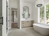 The primary bathroom features a soaking tub, two seperate custom vanities with ample storage, quartz countertops, and sleek fixtures—all designed for a spa-like experience at home.